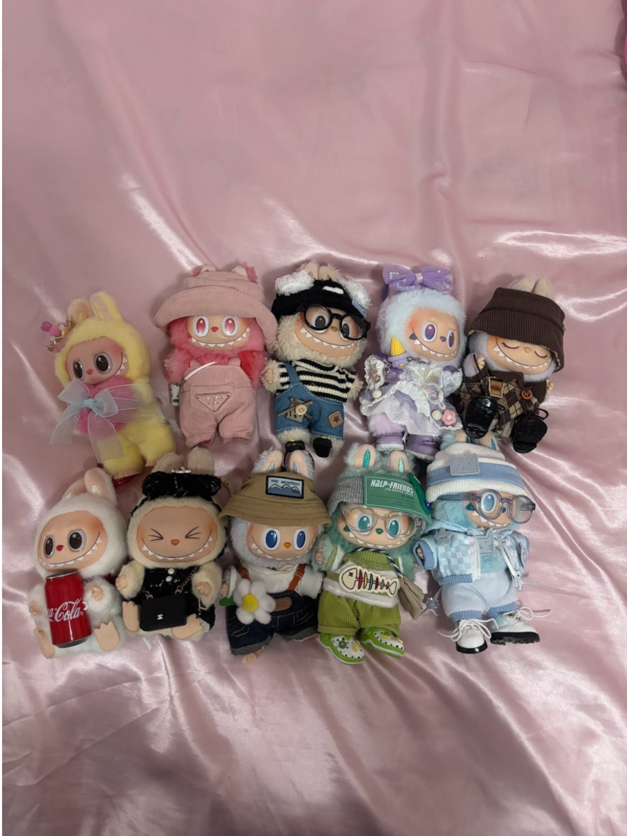 A collection of Labubu plush toys is displayed on a bed. The wide-eyed, toothy characters designed by Kasing Lung have gained viral popularity worldwide, even earning a parody in South Park’s Season 27 episode “Wok is Dead,” which portrayed the dolls as the center of a consumer craze and political satire.
